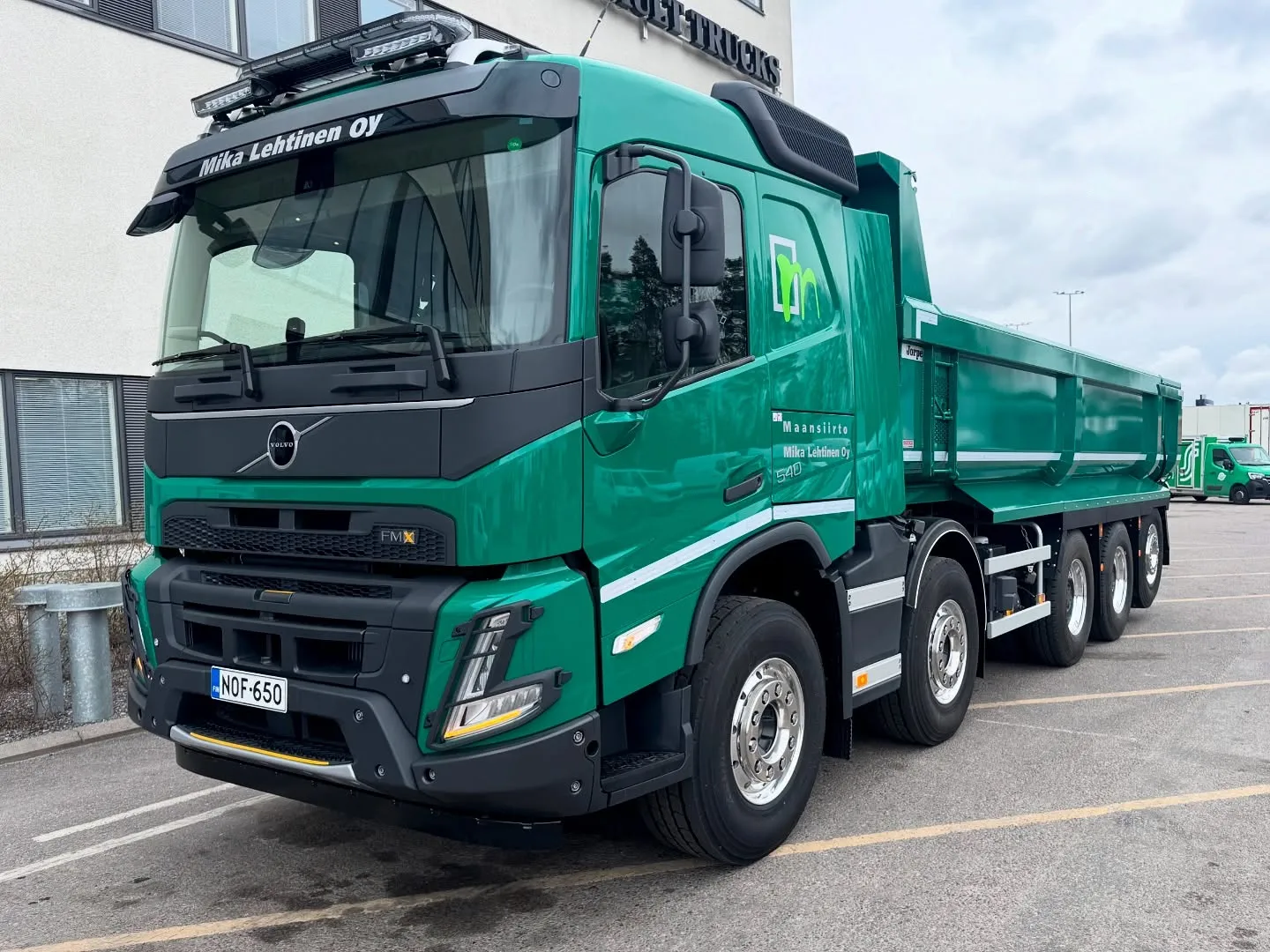 Kirkkaanvihreä Volvo FMX -kippiauto pysäköitynä ulkona, jossa näkyy yrityksen nimi "Mika Lehtinen Oy" ja rekisterinumero "NOF-650". Valoisa sää.